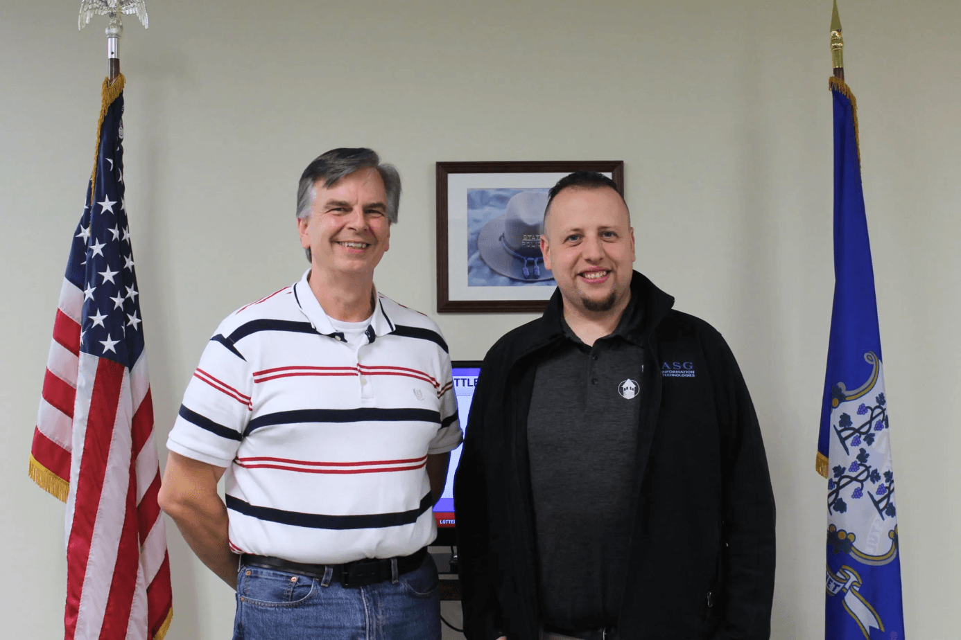 An ASG Information Technologies team member with a Connecticut client, standing between the U.S. and Connecticut state flags.